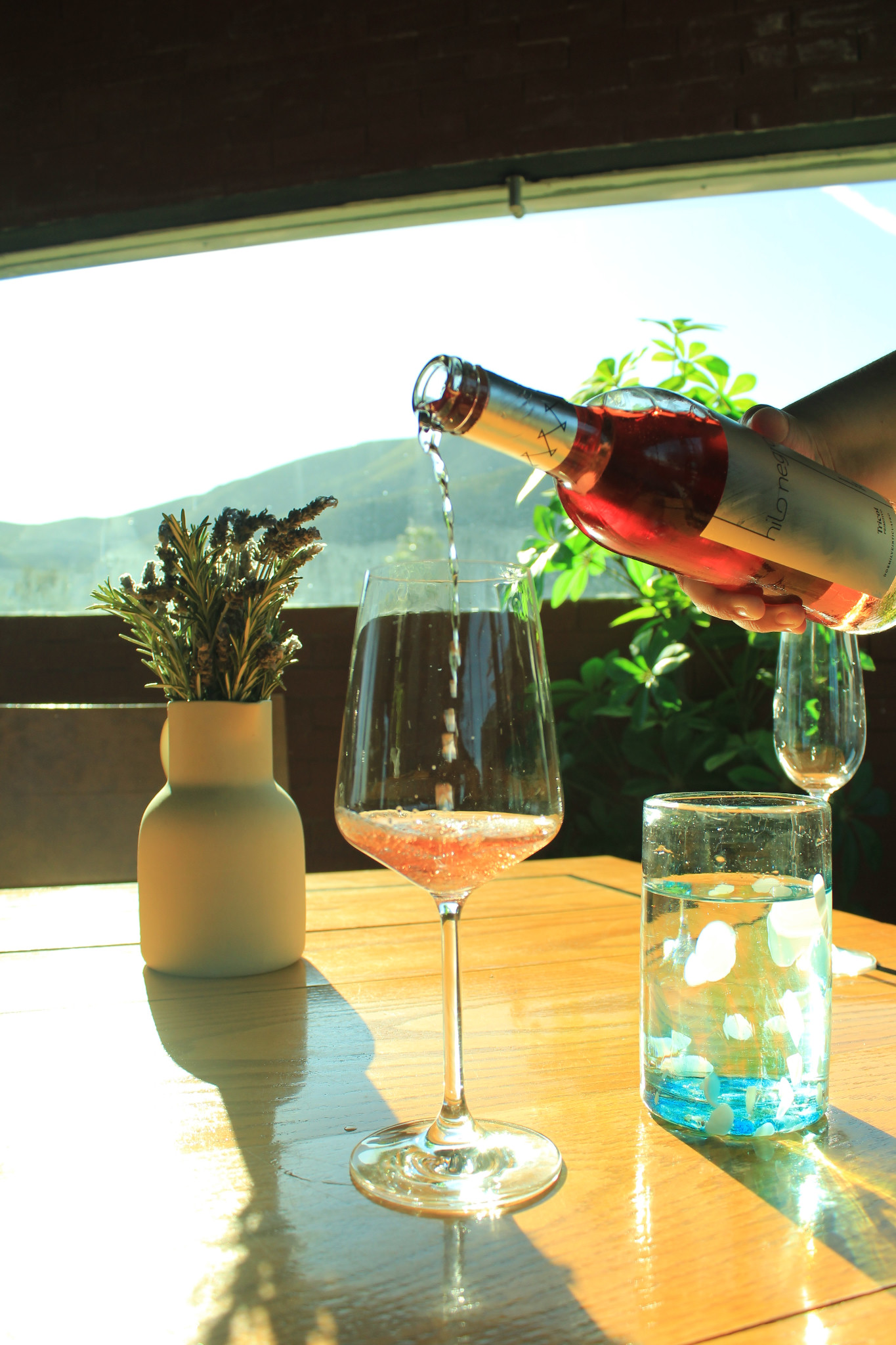 Vino rosado servido en una copa sobre una mesa soleada de EMAT, con las montañas al fondo.